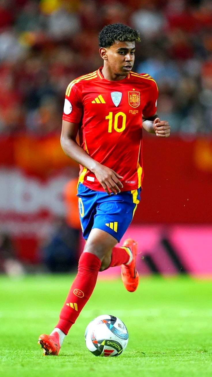A soccer player in a red and yellow Spain national team uniform with the number 10 is dribbling a ball on the field during a match, as blurred spectators watch—perfect action to catch live on Latino IPTV.
