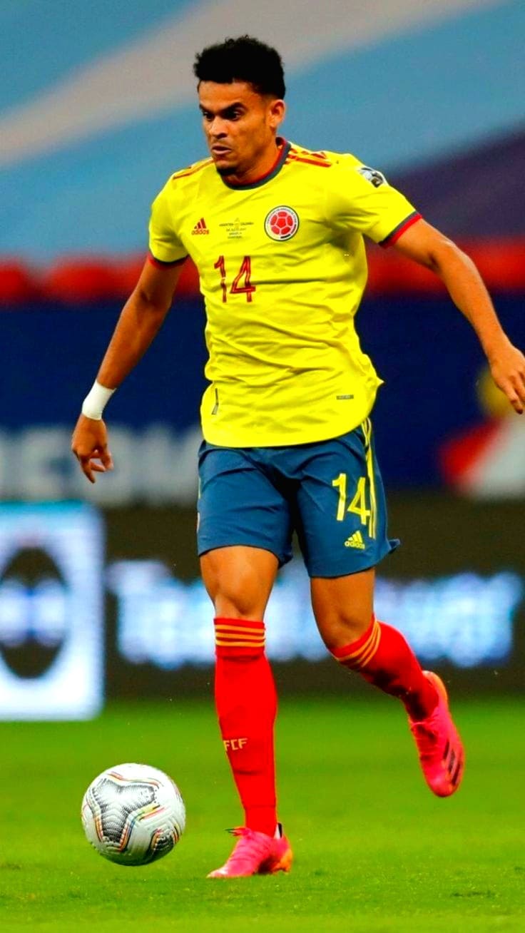 A soccer player in a yellow jersey with the number 14, blue shorts, and red socks runs with the ball during a match on a green field. The action-packed scene is perfect for streaming live on Latino IPTV.