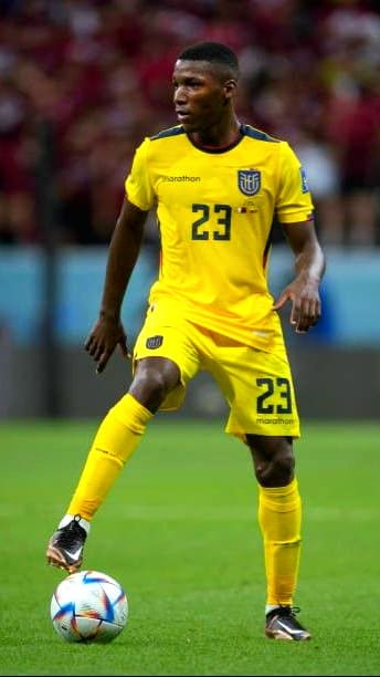 A soccer player in a yellow Ecuador national team uniform with number 23 controls a ball on the field during a match, which is broadcast live on Latino IPTV. The background shows a blurred crowd.