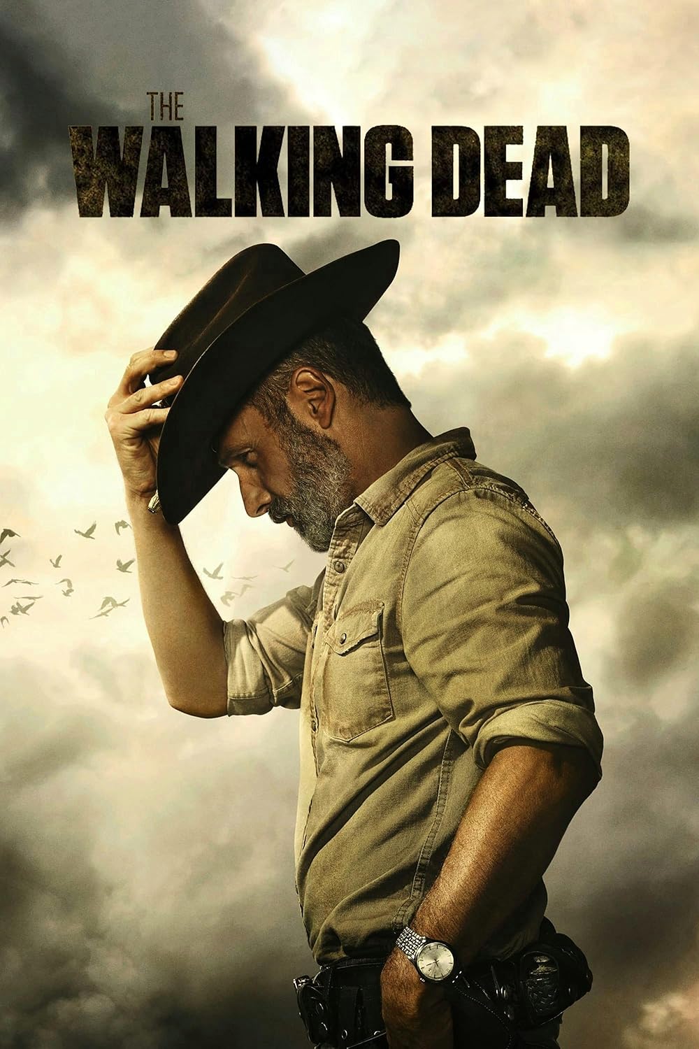 A man in a sheriff’s hat and tan shirt stands in profile under a dramatic cloudy sky, holding the brim of his hat. The title The Walking Dead appears above him, streaming on Latino IPTV. Birds are flying in the background.